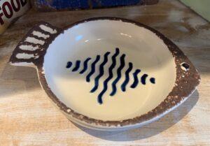 The Ceramic Fish plate with stripes features a small fish shape, rustic brown rim, and blue wavy centre lines - ideal as a nautical kitchen gift.